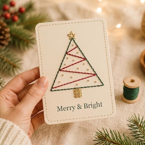 Könnte beinhalten: Eine rechteckige, cremefarbene Karte mit abgerundeten Ecken und genähten Rändern, die einen gestickten Weihnachtsbaum in Grün und Rot mit einem goldenen Stern an der Spitze und goldenen Perlen zeigt. Der Text Merry & Bright steht unten in Dunkelgrün.