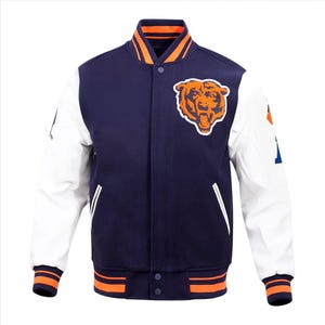 Puede incluir: Una chaqueta universitaria azul marino con mangas blancas, que presenta un logotipo de cabeza de oso naranja en el pecho izquierdo. La chaqueta tiene un cierre frontal de botones a presión, cuello, puños y dobladillo acanalados en naranja y azul.