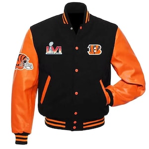 Op de afbeelding: Een zwart varsity jack met oranje mouwen, voorzien van een Super Bowl LVI-logo op de rechterborst, een Bengals teamlogo op de linkerborst en een tijgerhelm-afbeelding op de rechtermouw. Het jack heeft oranje drukknopen en gestreepte boorden.