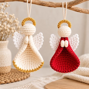 May include: Two crocheted angel ornaments hanging from a branch. One angel is cream-colored with a gold halo and hem, while the other is red with a cream-colored head, white wings, and a gold halo. Both feature small hands joined in front.