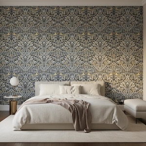 Op de afbeelding: Een slaapkamer met een bed voorzien van een crèmekleurig dekbed en een textuurrijke sprei, geplaatst tegen een muur met donker behang met een goud en grijs damastpatroon. Een ronde witte lamp staat op een gouden bijzettafel.