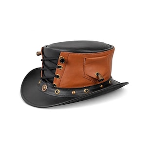 Puede incluir: Un sombrero de copa negro y marrón con corona plana y ala curva. El sombrero incluye un panel lateral marrón con un bolsillo pequeño, cordones negros con ojales de tono latón y una banda negra adornada con tachuelas y ojales metálicos.