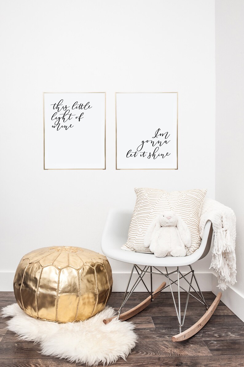 Pode incluir: Duas impress&otilde;es emolduradas com molduras douradas e fundos brancos. O texto nas impress&otilde;es diz "This little light of mine" e "I'm gonna let it shine". Uma cadeira de balan&ccedil;o branca com um travesseiro estampado em dourado e um coelho de pel&uacute;cia branco. Um pufe dourado fica em cima de um tapete branco e felpudo.