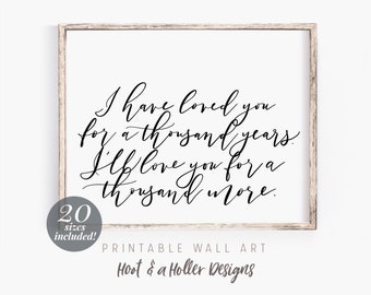 May include: Printable wall art with a black and white calligraphy quote that reads "I have loved you for a thousand years. I'll love you for a thousand more." The quote is framed in a light wood frame. The text "20 sizes included!" is in the lower left corner. The text "PRINTABLE WALL ART Hoot & a Holler Designs" is in the lower center.
