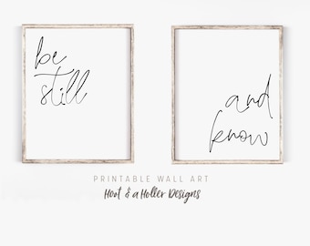 May include: Two framed wall art prints with a white background and black cursive text. The left print says "be still" and the right print says "and know". The frames are a light brown color. The bottom of the image says "Printable Wall Art" and "Host & a Holler Designs".