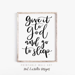May include: Black and white printable wall art with the text "Give it to god and go to sleep." The text is in a cursive font. The art is framed in a light wood frame.