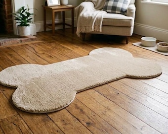 Op de afbeelding: Een beige, pluche vloerkleed in de vorm van een groot hondenbot. Het kleed heeft een zacht, getextureerd oppervlak met afgeronde randen, ontworpen om plat op de vloer te liggen. De neutrale kleur en het duidelijke silhouet van een bot zorgen voor een herkenbare vorm.