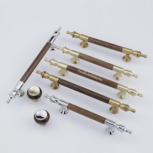 May include: A collection of cabinet hardware including five long bar pulls and two round knobs. The pulls feature dark brown wood centers with metallic ends in brass or chrome finishes. One pull displays the text HandlesWithStories in white.