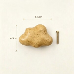 May include: A light brown wooden cabinet knob shaped like a cloud, featuring a smooth, natural wood grain finish. The knob measures 6.5 cm in width and 4.5 cm in height, accompanied by a single silver-toned metal mounting screw for installation.