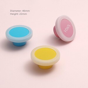Puede incluir: Tres pomos redondos para armarios en azul, amarillo y rosa con un borde blanco. El pomo rosa presenta el texto HWS. Cada pomo tiene un diámetro de 46 mm y una altura de 22 mm. Estas piezas circulares tienen un centro liso y sólido.