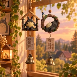 May include: Two hanging wind chimes featuring grey, round, furry creatures. One hangs from a wooden house frame, the other from a circular branch. Both have rectangular wooden plaques with Japanese text and brass bells suspended at the bottom.