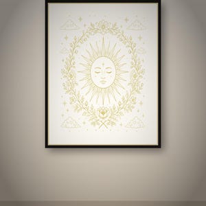 Peut inclure: Une impression d'art mural encadrée présentant une illustration au trait doré d'un soleil avec un visage humain, centrée dans une couronne ovale de fleurs et de feuilles. Le motif inclut de petites étoiles et des nuages sur un fond clair, le tout dans un cadre noir.