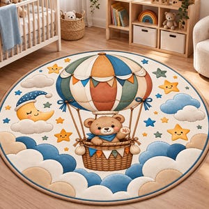 Op de afbeelding: Een rond vloerkleed met een centrale illustratie van een bruine teddybeer in een rieten mand van een heteluchtballon. Het ontwerp bevat een grote veelkleurige ballon, een lachende halve maan, diverse gele sterren en blauwe en beige wolken.