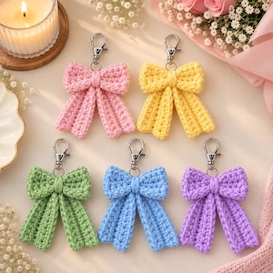 May include: Five crochet bow keychains in pastel colors including pink, yellow, light green, light blue, and purple. Each bow features a central knot and two hanging tails, attached to a silver-toned metal lobster clasp swivel hook.