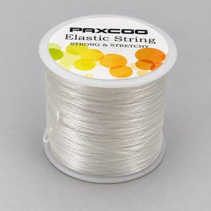 May include: A spool of clear elastic string by PAXCOO. The white label on top features the text PAXCOO Elastic String STRONG & STRETCHY with a graphic of overlapping yellow and orange circles. The string is wound around a clear plastic spool.