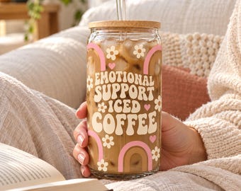 May include: A clear glass tumbler with a bamboo lid and glass straw, filled with iced coffee. The exterior features white, pink, and brown graphics of rainbows, flowers, and hearts with the text "EMOTIONAL SUPPORT ICED COFFEE".