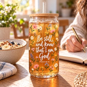 May include: A clear glass tumbler with a bamboo lid and a glass straw, filled with amber liquid. The exterior features a colorful floral pattern and the white text: Be still, and know that I am God, PSALM 46:10.