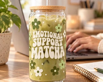 May include: A clear glass tumbler with a bamboo lid and a glass straw, filled with a green matcha beverage. The exterior features white text that reads Emotional Support Matcha, surrounded by various shades of green and white flower icons.