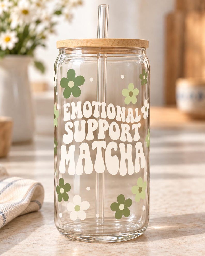 Digital mockup of a clear glass cup showing Emotional Support Matcha lettering with green and ivory flowers. Bamboo lid shown.