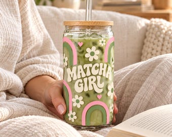 May include: A clear glass tumbler filled with a green matcha beverage, featuring a bamboo lid and a glass straw. The exterior is decorated with white flowers, pink hearts, and green and pink rainbows, with the text "MATCHA GIRL" in white.