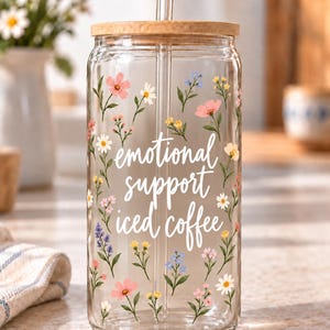 Digital mockup of a clear glass cup showing Emotional Support Iced Coffee script and delicate multicolor wildflowers. Bamboo lid shown.