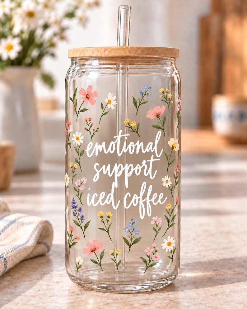 Digital mockup of a clear glass cup showing Emotional Support Iced Coffee script and delicate multicolor wildflowers. Bamboo lid shown.