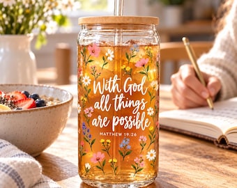 May include: A clear glass tumbler with a bamboo lid and glass straw, filled with amber liquid. The exterior features a colorful floral pattern and white script text that reads With God all things are possible MATTHEW 19:26.