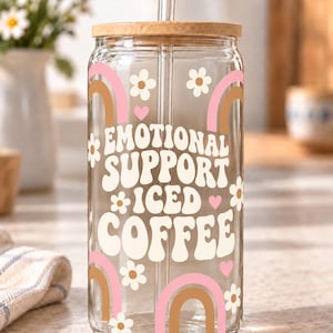 Digital mockup of a clear glass cup showing cream Emotional Support Iced Coffee lettering, pink and brown rainbows and white daisies. Bamboo lid shown.
