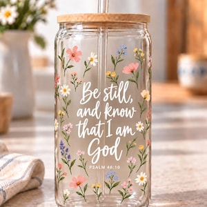 Digital mockup of a clear glass cup showing Be Still and Know That I Am God lettering and Psalm 46:10 among wildflowers. Bamboo lid shown.