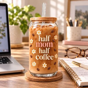 Half Mom Half Coffee glass cup with daisies and coffee beans, bamboo lid and glass straw — desk scene.