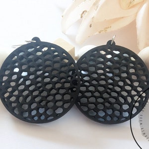 May include: A pair of black circular earrings with a honeycomb pattern. The earrings are made of a lightweight material and have a modern design.