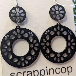 May include: Black dangle earrings with a floral design. The earrings are made of laser cut acrylic and have a silver hook.