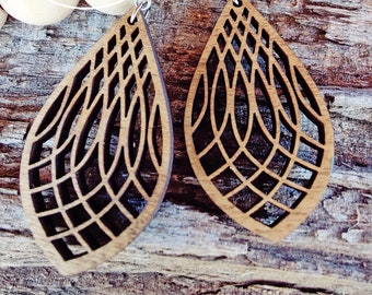 Puede incluir: Un par de pendientes de madera con un diseño geométrico. Los pendientes son marrones y tienen un patrón delicado e intrincado. Están colgados de ganchos plateados.