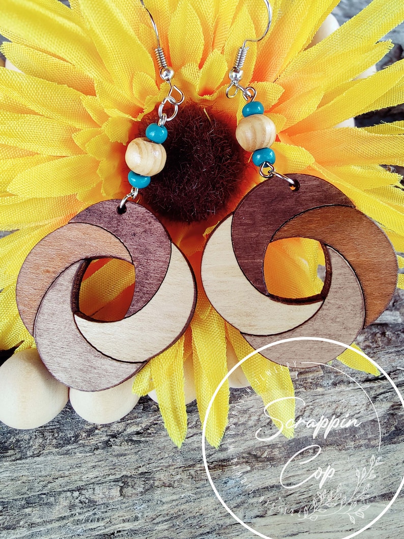 May include: A pair of wooden earrings with a unique knot design. The earrings are made of three different shades of wood, creating a layered effect. The earrings are accented with turquoise and wooden beads.