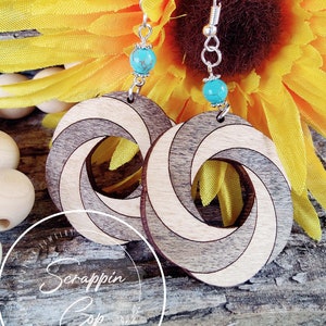 May include: A pair of wooden earrings with a spiral design. The earrings are made of light and dark wood and have a turquoise bead on each earring. The earrings are hanging from silver hooks.
