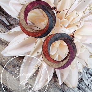 May include: A pair of wooden earrings with a spiral design. The earrings are made of multiple shades of brown and purple wood. The earrings are hanging from copper hooks.