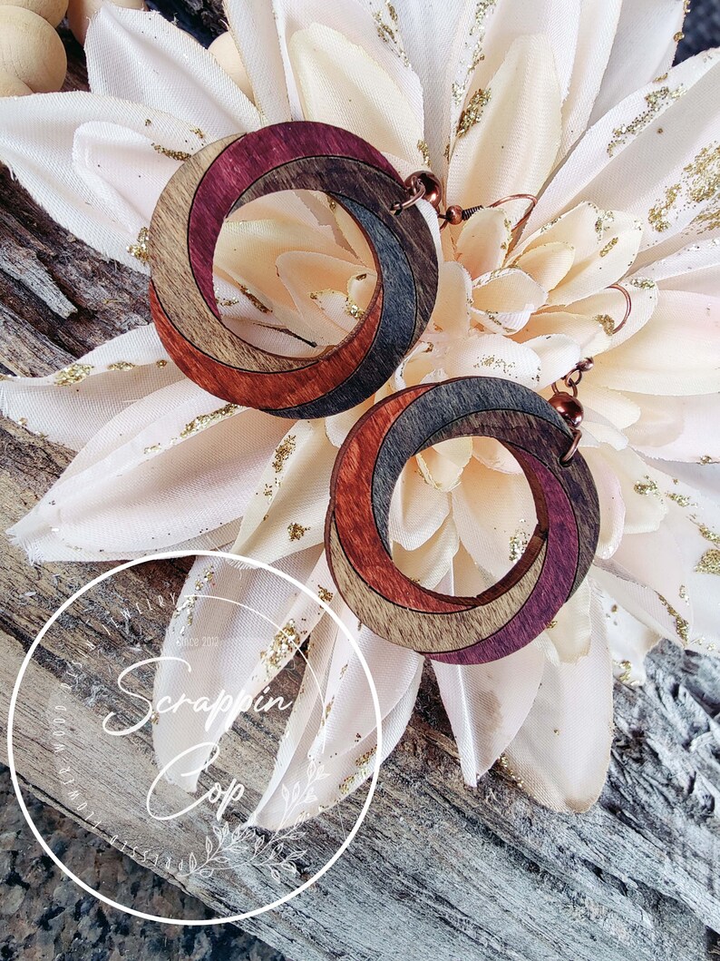 May include: A pair of wooden earrings with a spiral design. The earrings are made of multiple shades of brown and purple wood. The earrings are hanging from copper hooks.