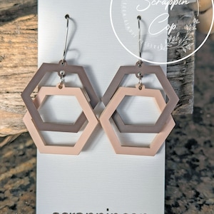 May include: A pair of earrings with a double hexagon design. The hexagons are in shades of brown and pink. The earrings are on a white card with the text "scrappincop" printed on it.