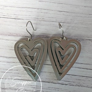 Puede incluir: Un par de pendientes de plata con un dise&ntilde;o de coraz&oacute;n superpuesto. Cada pendiente tiene tres corazones, uno dentro del otro, creando un aspecto &uacute;nico e intrincado.