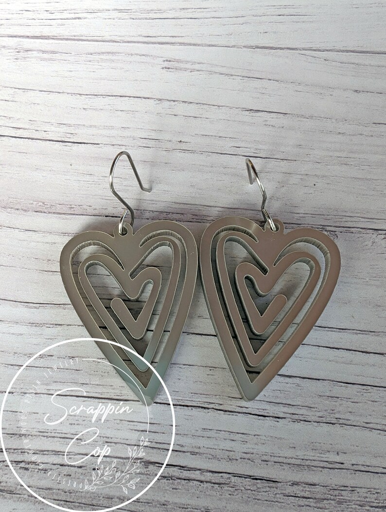 Puede incluir: Un par de pendientes de plata con un dise&ntilde;o de coraz&oacute;n superpuesto. Cada pendiente tiene tres corazones, uno dentro del otro, creando un aspecto &uacute;nico e intrincado.