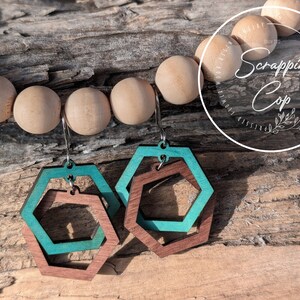 May include: Teal and brown wooden hexagon earrings with a layered design. The earrings are hanging from silver hooks.