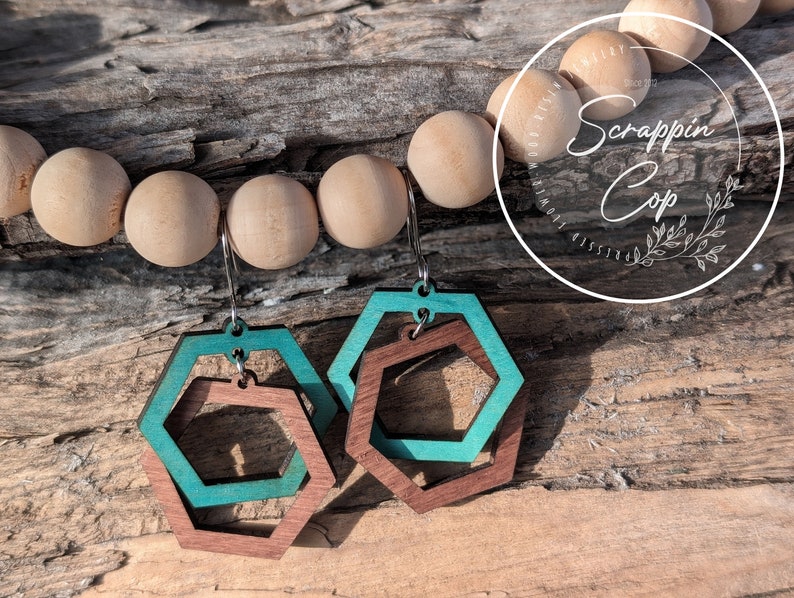 May include: Teal and brown wooden hexagon earrings with a layered design. The earrings are hanging from silver hooks.