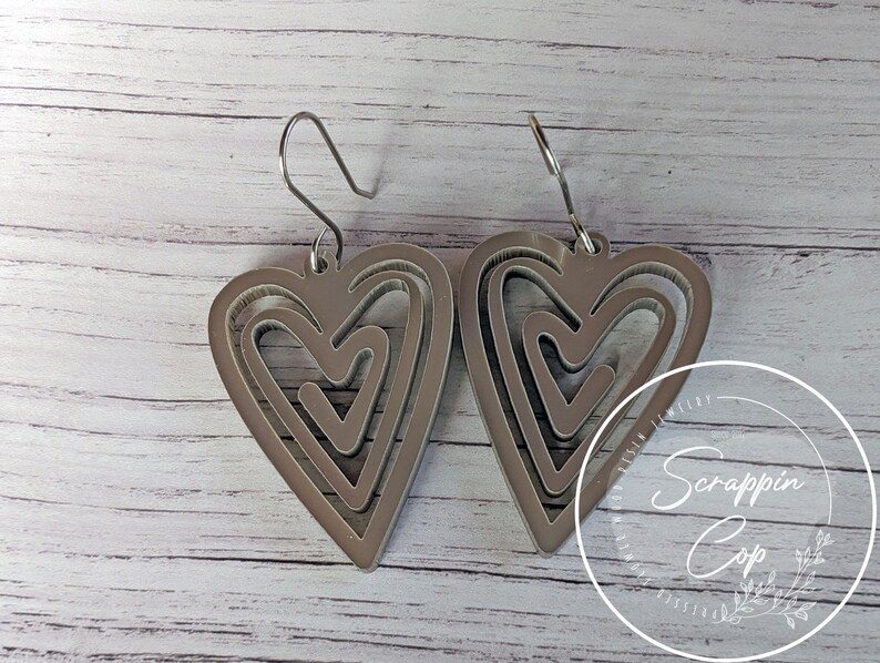 Puede incluir: Un par de pendientes de plata con un dise&ntilde;o de coraz&oacute;n en capas. Los corazones est&aacute;n superpuestos, creando un efecto tridimensional.