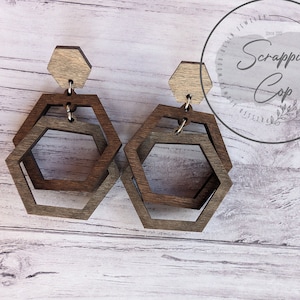May include: A pair of wooden earrings with a hexagonal shape. The earrings are made of two layers of wood, with the top layer being a lighter color than the bottom layer.
