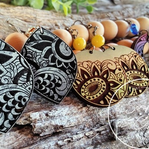May include: A set of four pairs of wooden earrings with intricate mandala designs. The earrings are in various colors, including black, white, brown, yellow, and rainbow.