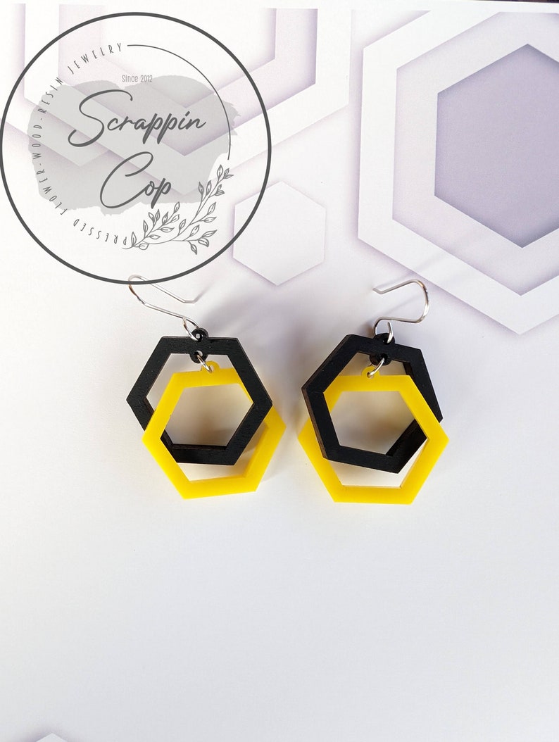 May include: A pair of yellow and black hexagon shaped earrings. The earrings are made of acrylic and have a geometric design.