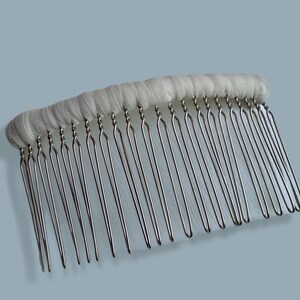 May include: A bridal hair comb with a row of silver-colored metal teeth attached to a white fabric base. The comb's teeth are evenly spaced and slightly curved. The fabric base is a soft, off-white color.