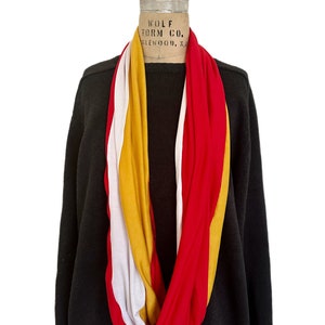 K&ouml;nnte beinhalten: Ein mehrfarbiger Infinity-Schal in Rot, Wei&szlig; und Gold ist &uuml;ber einem schwarzen Pullover auf einer Schaufensterpuppe drapiert. Der Schal ist aus einem weichen, flie&szlig;enden Stoff gefertigt. Die Schaufensterpuppe hat ein Vintage-Label von Wolf Form Co.