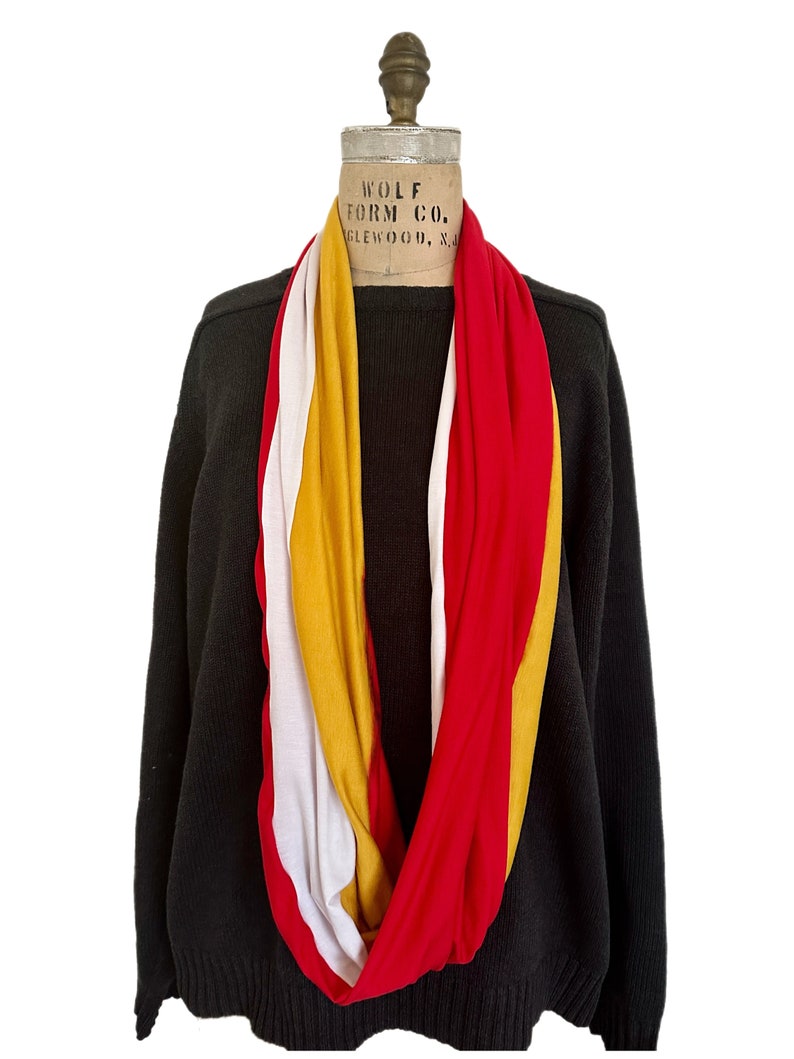 K&ouml;nnte beinhalten: Ein mehrfarbiger Infinity-Schal in Rot, Wei&szlig; und Gold ist &uuml;ber einem schwarzen Pullover auf einer Schaufensterpuppe drapiert. Der Schal ist aus einem weichen, flie&szlig;enden Stoff gefertigt. Die Schaufensterpuppe hat ein Vintage-Label von Wolf Form Co.