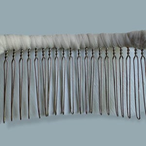 May include: A vintage hair comb with a white, fabric-wrapped top and silver-toned metal teeth. The teeth are evenly spaced and have a looped design at the top. The comb is designed for securing hair in place.